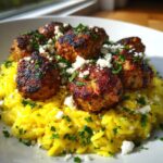 Close-up of perfectly seared greek chicken meatballs served over bright yellow lemon orzo, topped with feta and parsley.