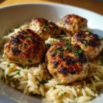 Close-up of four seared greek chicken meatballs served over creamy orzo pasta garnished with parsley.