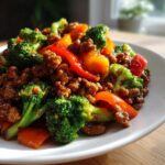 A close-up of a serving of ground beef stir fry mixed with bright green broccoli florets and slices of red and orange bell pepper.