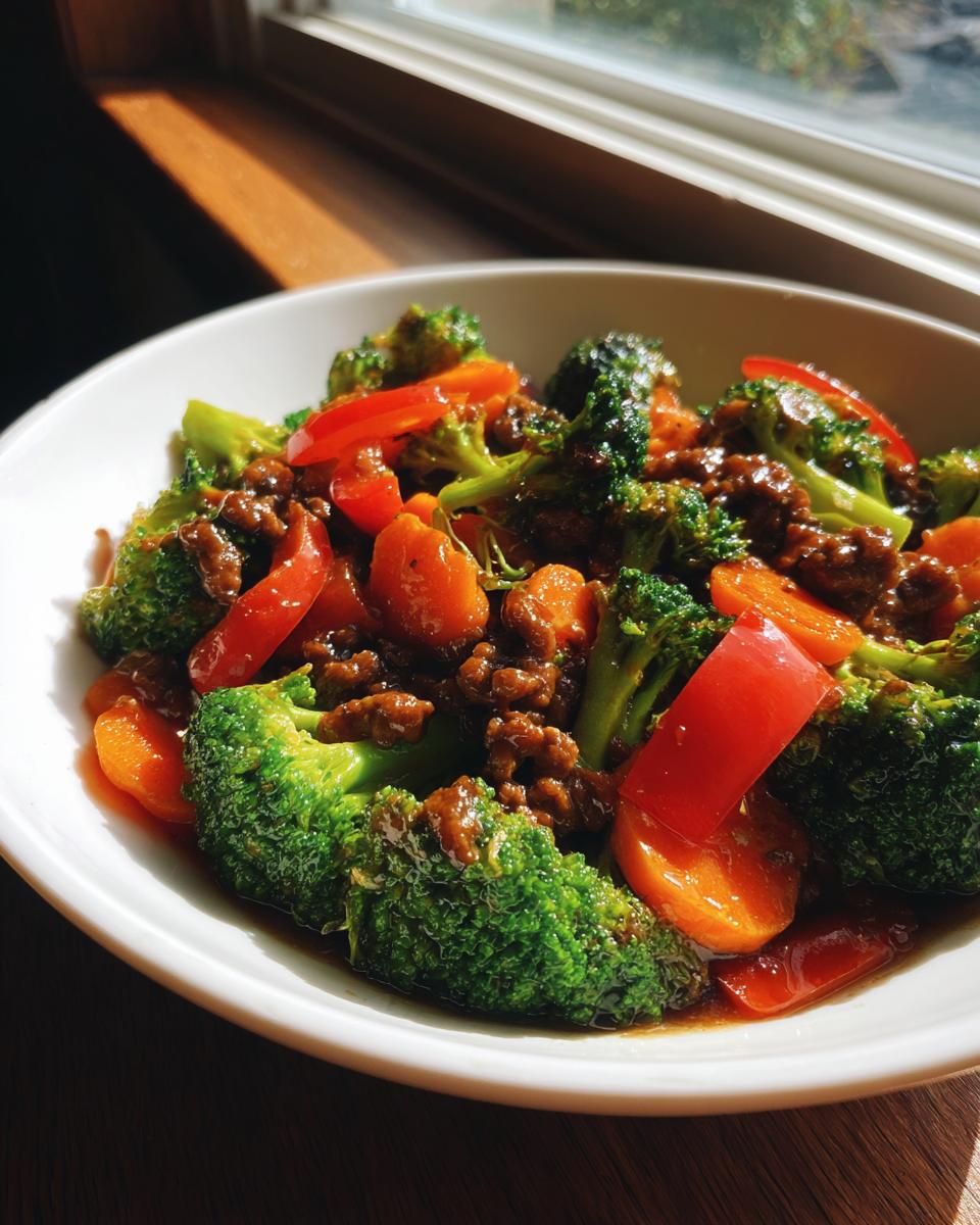 A close-up of a white bowl filled with a vibrant ground beef stir fry featuring bright green broccoli, orange carrots, and red bell peppers.