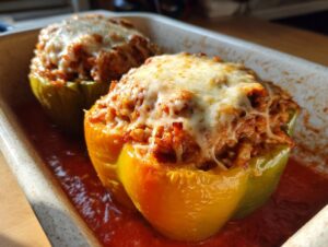 Two baked ground turkey stuffed peppers, topped with melted cheese, sitting in tomato sauce in a baking dish.