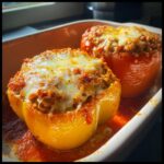 Two baked ground turkey stuffed peppers, one yellow and one red, topped with melted cheese in a baking dish with tomato sauce.