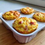 Four freshly baked ham and cheese egg muffins with golden tops sitting in a white baking dish.