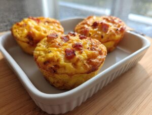 Three freshly baked ham and cheese egg muffins sitting in a small white rectangular baking dish.