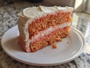 A close-up of a slice of moist Hawaiian guava cake with two layers of pink cake and white frosting.