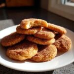 A stack of golden homemade churro cookies generously coated in cinnamon sugar, with one cookie broken open showing the soft interior.