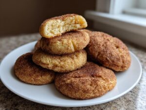 A stack of soft, round homemade churro cookies generously coated in cinnamon sugar, with one cookie broken open to show the texture.