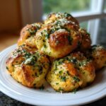 A stack of golden brown homemade garlic knots generously topped with melted butter, fresh parsley, and grated Parmesan cheese.