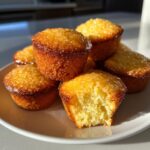 A stack of golden honey butter cornbread poppers, one bitten, glistening with a sweet glaze.
