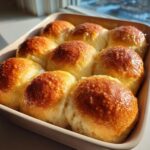 Close-up of golden brown, glossy irresistible dinner rolls baked together in a light ceramic baking dish.