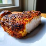 Close-up of a thick, juicy baked pork chop showing a perfectly seasoned, dark orange crust and moist white interior.