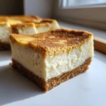 A single, thick slice of keto apple cheesecake bars showing a rich, creamy white filling and a brown crust, dusted with cinnamon.