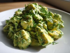 A close-up serving of creamy keto avocado egg salad mixed with chunks of egg and topped generously with fresh dill.