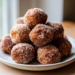 A close-up stack of freshly made keto cinnamon donut holes heavily coated in cinnamon sugar.