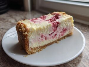 A thick slice of keto strawberry cheesecake featuring a creamy white filling swirled with bright pink strawberry puree and a thick crumb crust.