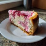 A close-up of a slice of keto strawberry cheesecake with a vibrant pink swirl on a white plate.