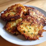 A stack of golden-brown, crispy leftover mashed potato pancakes garnished with fresh chives on a white plate.