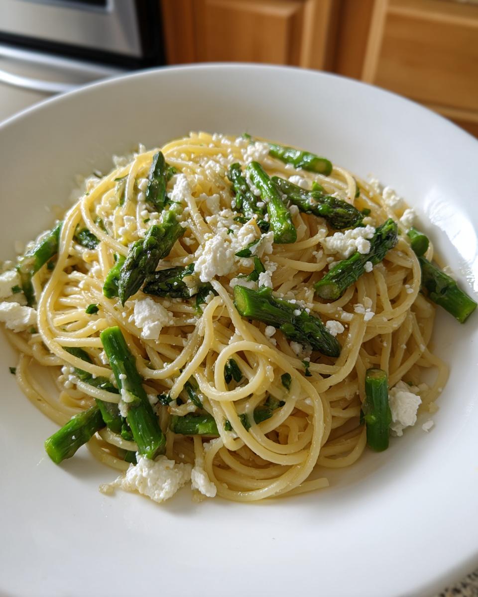 A close-up of a bowl of lemon capellini salad tossed with bright green asparagus pieces and crumbled white cheese.
