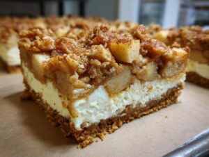 A thick slice of loopy whisk gluten free apple cheesecake bars showing the graham crust, creamy filling, and apple crumble topping.