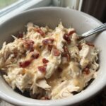 Close-up of shredded chicken mixed with melted cheese and topped with bacon bits, representing low carb easy pepper jack crack chicken.