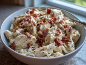 A close-up of shredded chicken coated in creamy sauce and topped with bacon bits, representing low carb easy pepper jack crack chicken.