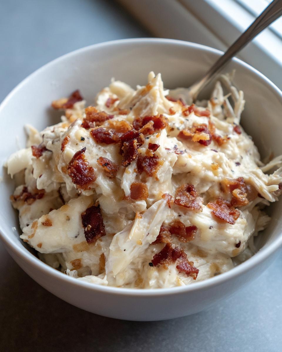 A white bowl filled with creamy, shredded low carb easy pepper jack crack chicken topped with crispy bacon bits.