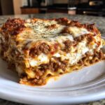 A thick, layered slice of million dollar lasagna featuring rich meat sauce and creamy cheese on a white plate.