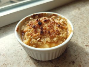Close-up of a single serving of golden brown mini apple crisps baked in a white ramekin.