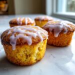 Close-up of a moist mini lemon cake topped with dripping lavender glaze, part of a batch of mini lemon cakes with lavender glaze.