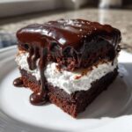 Close-up of a rich slice of Mississippi Mud Cake featuring dark chocolate layers and white marshmallow filling, topped with dripping chocolate ganache.