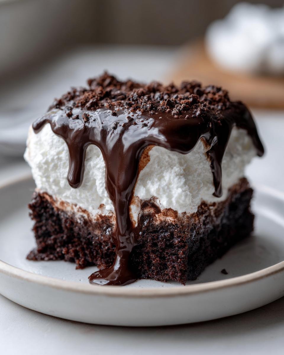 Close-up of a rich slice of Mississippi Mud Cake topped with whipped cream, chocolate fudge drizzle, and cookie crumbs.