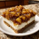 A single serving of no bake apple cheesecake bars featuring a graham cracker crust, creamy white filling, and cinnamon apple topping.