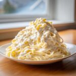 A tall mound of fettuccine pasta smothered in rich, creamy sauce, resembling an olive garden alfredo copycat.