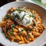 Close-up of one pot sun-dried tomato pasta topped with a dollop of whipped ricotta and fresh basil.