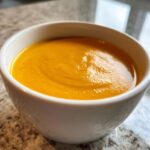 Close-up of a white bowl filled with smooth, vibrant orange panera butternut squash soup.