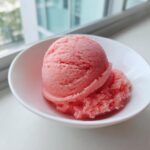 A close-up of two scoops of bright pink 2-ingredient summer sherbet in a small white bowl.