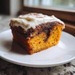 Close-up of a single serving slice of moist pumpkin cinnamon roll cake topped with thick cream cheese frosting.