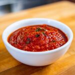 Close-up of rich, chunky Rao's marinara sauce garnished with herbs in a white bowl.