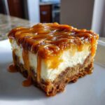 A close-up of a thick slice of salted caramel apple cheesecake bars topped with rich, dripping caramel sauce.