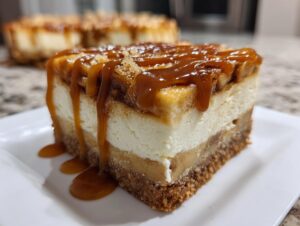 A thick slice of salted caramel apple cheesecake bars showing three distinct layers and drizzled heavily with caramel sauce.