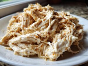 Close-up of creamy, shredded crockpot olive garden chicken piled high on a white plate.