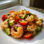 Close-up of a vibrant shrimp avocado salad featuring seasoned shrimp, diced avocado, halved cherry tomatoes, and red onion slices.