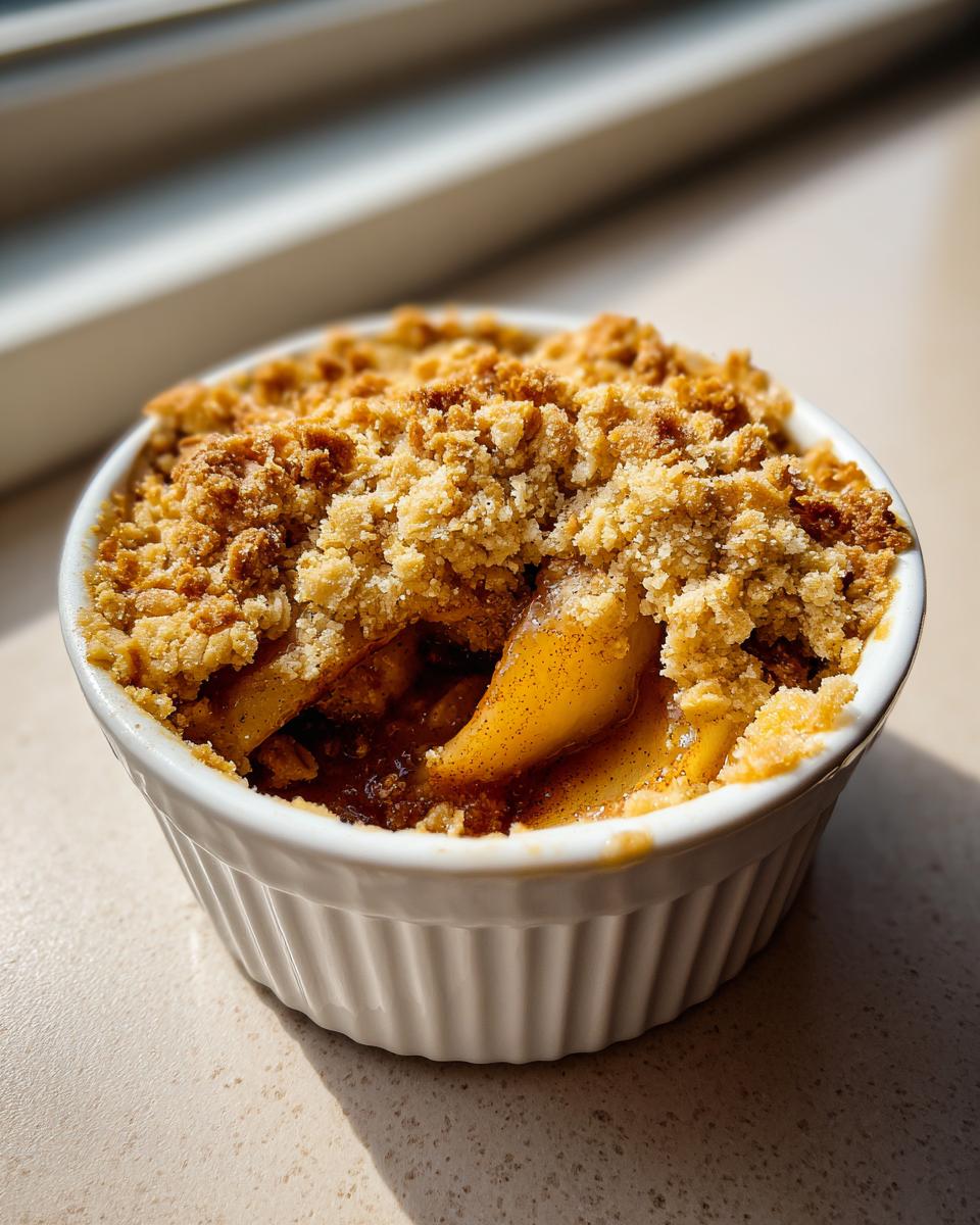 A single serving of warm mini apple crisps in a white ramekin with a golden brown crumble topping.