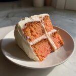 A moist slice of pink layered hawaiian guava cake with thick white cream cheese frosting on a small plate.