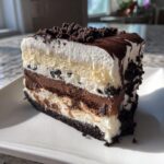 A decadent slice of homemade dairy queen ice cream cake showing layers of vanilla and chocolate ice cream, cookie crumble, and fudge topping.