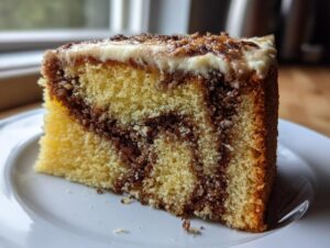 Close-up of a moist slice of sock-it-to-me cake showing yellow cake swirled with brown streusel filling and topped with white frosting.
