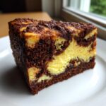A close-up of a rich, marbled slice of sock-it-to-me cake showing dark chocolate cake and yellow cream cheese swirls.