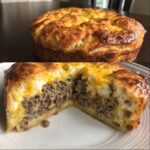 A cross-section view of a baked southern style cheeseburger pie showing a ground beef filling topped with mashed potatoes and melted cheddar cheese.