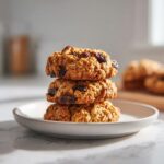 A stack of three freshly baked oatmeal raisin cookies resting on a small white plate.