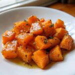 Close-up of tender, glazed cubes of braised butternut squash seasoned with fresh thyme leaves.